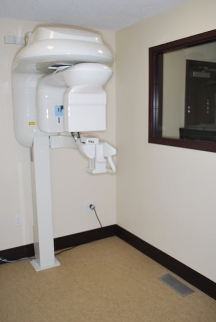 Clinical operatory featuring a gray patient chair and wall-mounted diagnostic equipment.