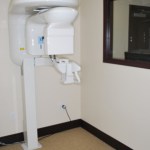 Clinical operatory featuring a gray patient chair and wall-mounted diagnostic equipment.