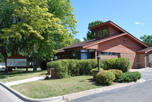 Exterior of a modern brown and brick office building surrounded by green trees and landscaping.