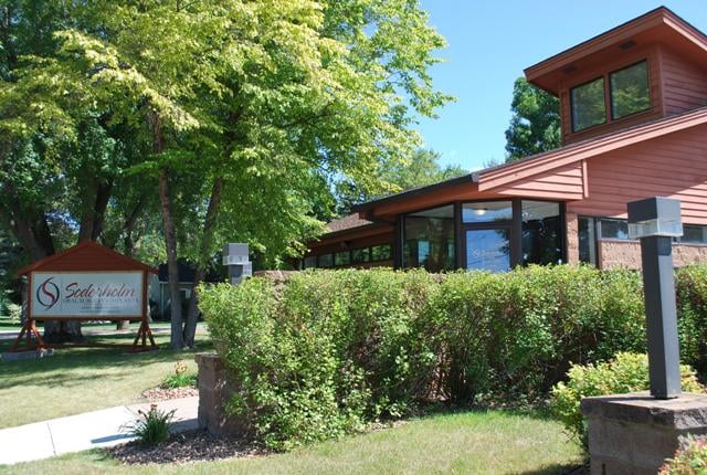 Wide shot of a professional office building with a prominent sign and manicured bushes.