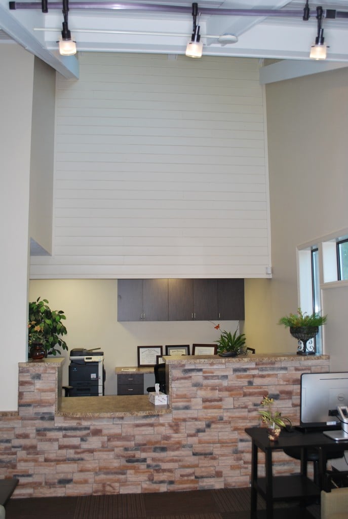 View of an office reception area with high ceilings, track lighting, and a stone-front desk.