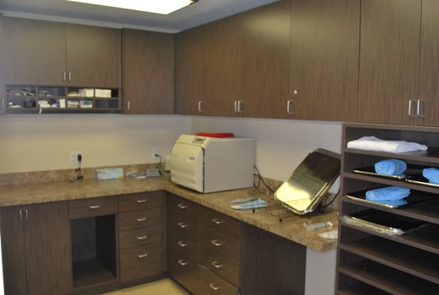 Professional sterilization room with wood cabinets, stone counters, and a benchtop autoclave.