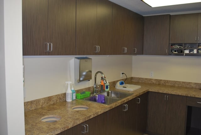 Medical laboratory area with a stainless steel sink, brown cabinets, and integrated countertop waste chutes.