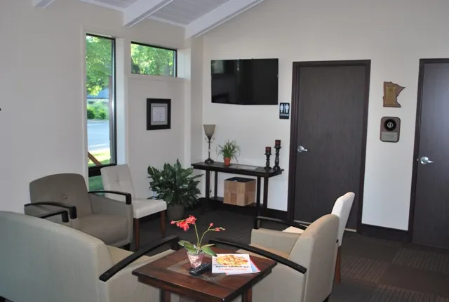Cozy waiting room area with comfortable armchairs, a side table, and a wall-mounted television.