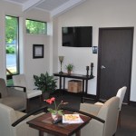 Cozy waiting room area with comfortable armchairs, a side table, and a wall-mounted television.