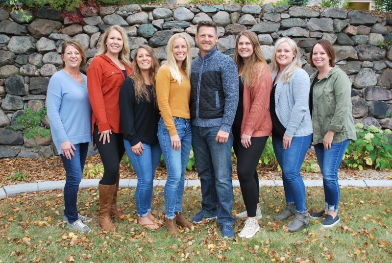 A smiling professional team posing together outdoors in front of a stone wall.